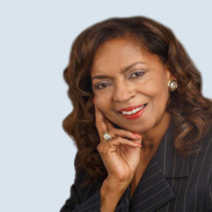 Olivet is an African-American woman. She has medium length drank brown hair with highlights. She is wearing a green jacket and is smiling with a pleasant pose. She is pictured in front of a blue-grey background.